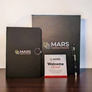 Premium appreciation box open showing branded notebook, metal pen, and greeting card